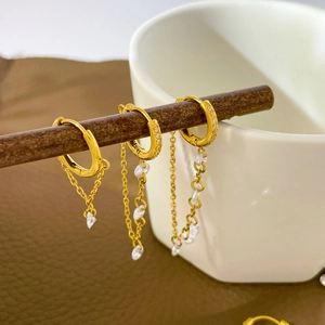 Detailed view of three gold tassel earrings with zircons hanging on a wooden stand