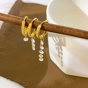 Macro detail of three gold tassel earrings with cubic zirconia on a wooden stand