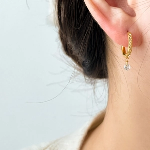 Detailed close-up of gold hoop earring with zircon tassel on a model side profile