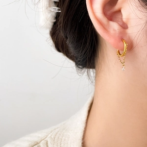 Close-up of gold titanium steel hoop earring with tassel chain and zircon drop on ear