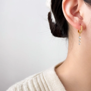 Detail of gold tassel earrings with zircon studs shown on a model's ear in close-up