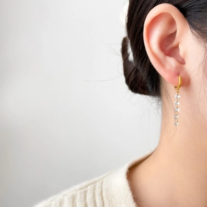 Detail of long tassel earrings with 18K gold plating and sparkling zircon stones on model