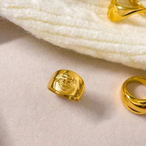 Gros plan d'une large bague en acier plaqué or 18K avec détail de relief de lèvres en 3D