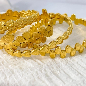 Golden 18K plated floral bangle set with flower and leaf patterns on white fabric
