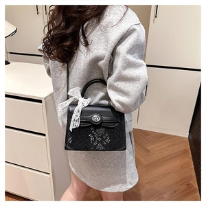 Detail of black snake pattern handbag with metal clasp and white lace bow decoration