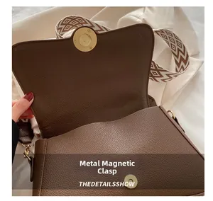 Detail einer braunen Tasche mit Litschimuster, Magnetverschluss und breitem Schultergurt