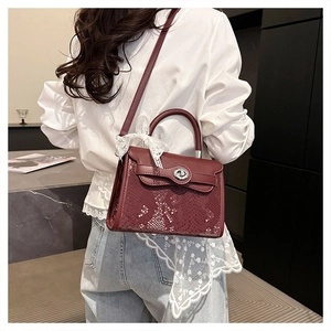 Detail view of dark red croc-embossed kelly bag worn by a model in casual style