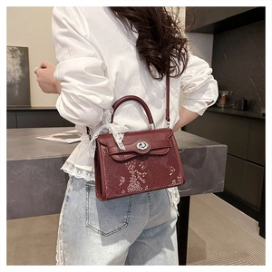Detail of burgundy leather handbag featuring snake-print flap and lace scarf on handle