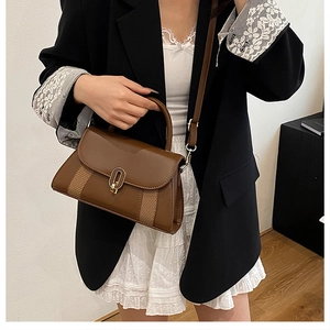 Détail d'un sac bandoulière marron avec des panneaux en tissu et un fermoir en métal doré