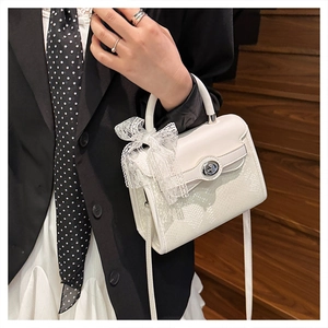 Detail of white snake-embossed Kelly bag with silver twist lock and lace bow decoration