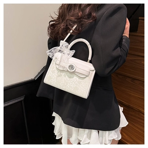 Detail of white handbag featuring a large lace bow and elegant silver twist lock
