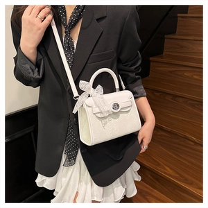 Detail of white snakeskin texture handbag featuring a lace bow and metal twist lock closure