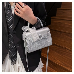 Macro detail of silver snake-textured handbag featuring white lace bow and metal lock