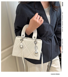 Detail of white quilted crossbody bag with silver hardware and spherical metal charm