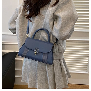 Détail du sac bandoulière en cuir bleu foncé avec serrure ovale en métal sur un mannequin