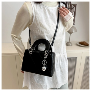 Detail of black quilted square bag with silver spherical charm on model in minimalist setting