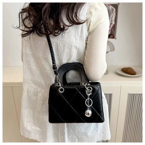 Detail showing the quilted black crossbody bag with silver ball charm and leather strap