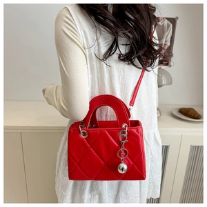 Detail of red quilted leather handbag with silver sphere charm worn as a crossbody bag