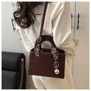 Detail of burgundy quilted handbag with elegant silver metal sphere charm and stitching