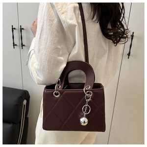Model trägt eine weinrote Stepptasche mit silbernem Kugelanhänger und harten Griffen