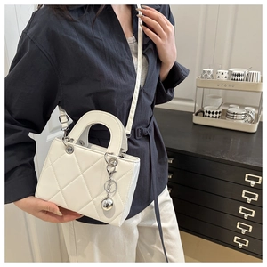 Chic white quilted crossbody bag with silver charm shown in a minimalist vintage setting