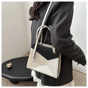 Detail view of structured geometric patchwork handbag worn by a model in black and beige