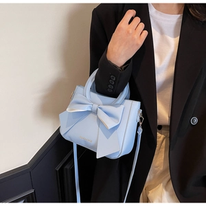 Detail of light blue bow handbag with matte leather finish and golden lettering