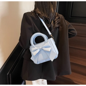 Detail of light blue bow handbag with rounded handle shown in a lifestyle street setting
