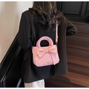 Detail view of pink bow handbag featuring a logo print and crossbody strap in elegant setting