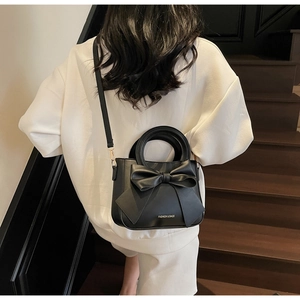 Close-up of black leather square bag with large bow and Fashion & Bags text print
