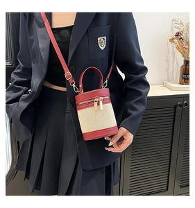 Detail of a chic cylinder bucket bag with beige weave and red leather trim shown on a model