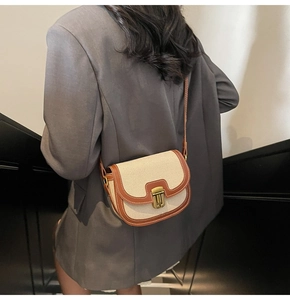 Detailed view of canvas saddle bag with brown leather trim worn as a shoulder bag