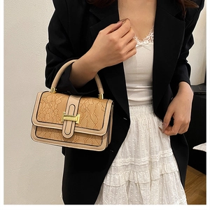 Detail of a beige handbag featuring delicate lace texture and a sleek metallic H-shaped clasp