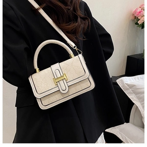 Close-up of cream textured handbag featuring gold H-shaped clasp on elegant black suit