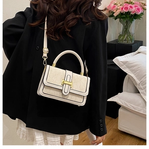 Detail of elegant beige lace-embossed crossbody bag with golden H-clasp on black blazer