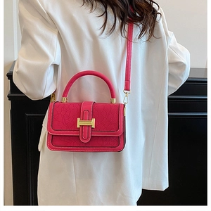 Detail of rose pink embossed handbag with floral texture and gold lock on white blazer