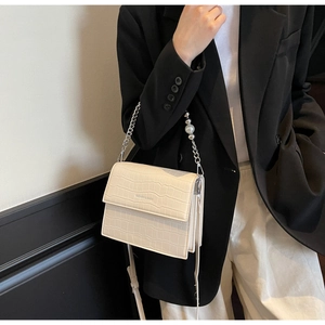Detail of off-white crocodile texture bag with large pearl and silver chain strap