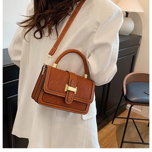 Brown leather handbag with lace embossing and gold buckle worn by model from the side