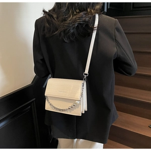 Detail of cream crossbody bag with crocodile texture and decorative pearl chain strap