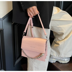 Pink croc-embossed crossbody bag with pearl chain detail worn with a black blazer