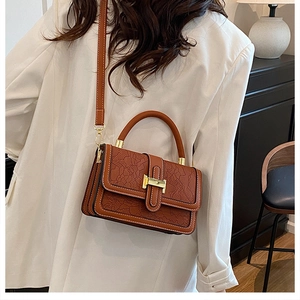 Detail of vintage brown crossbody bag with lace embossing on a model in white blazer
