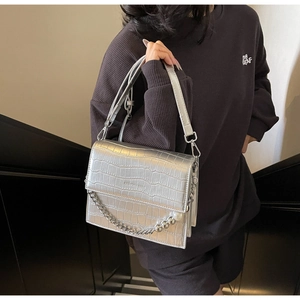Close-up of silver crocodile embossed handbag with metal chain and large pearl detail