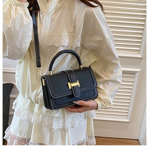 Detail of elegant black crossbody bag with gold H clasp and white contrast stitching