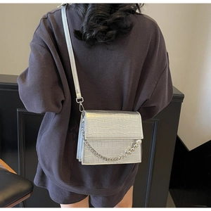 Detail of silver crocodile-textured bag featuring a metallic chain with pearl accents