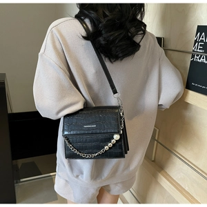 Detail of black crocodile pattern crossbody bag with pearl and silver bead chain strap