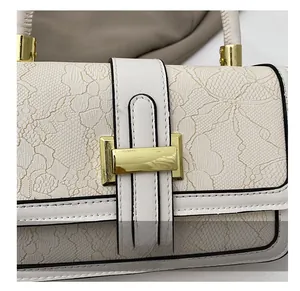 Detailed close-up of cream leather shoulder bag with lace embossing and gold metal buckle