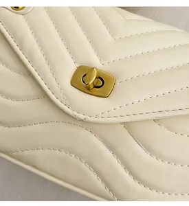 Detail of V-quilted faux leather and golden turn-lock closure on a creamy shoulder bag