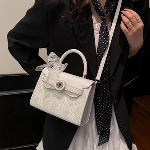 White trapezoid handbag with snakeskin texture and lace bow on black suit background