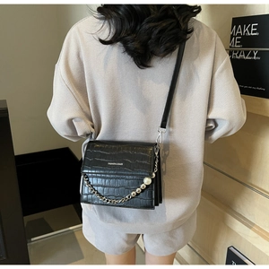 Detail of black faux leather crossbody bag with crocodile texture and pearl chain