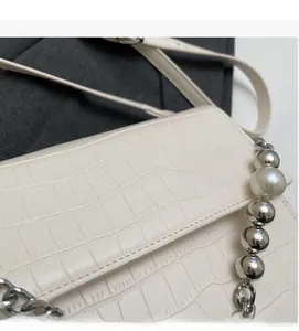 Close-up of white crocodile pattern shoulder bag with a beaded pearl chain decoration